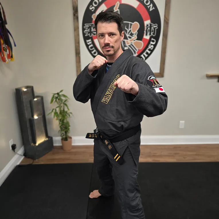 Vanguard instructor in a black gi demonstrating a ready stance inside the dojo