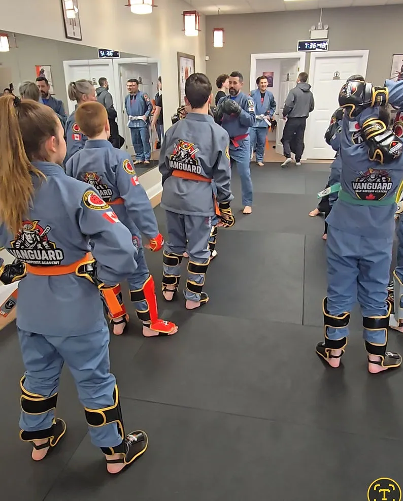 Older youth in blue Vanguard gis and protective gear gathering for a teen class drill