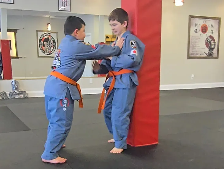 Two youth students in blue gis practicing a standing self-defense grip drill in the Vanguard dojo